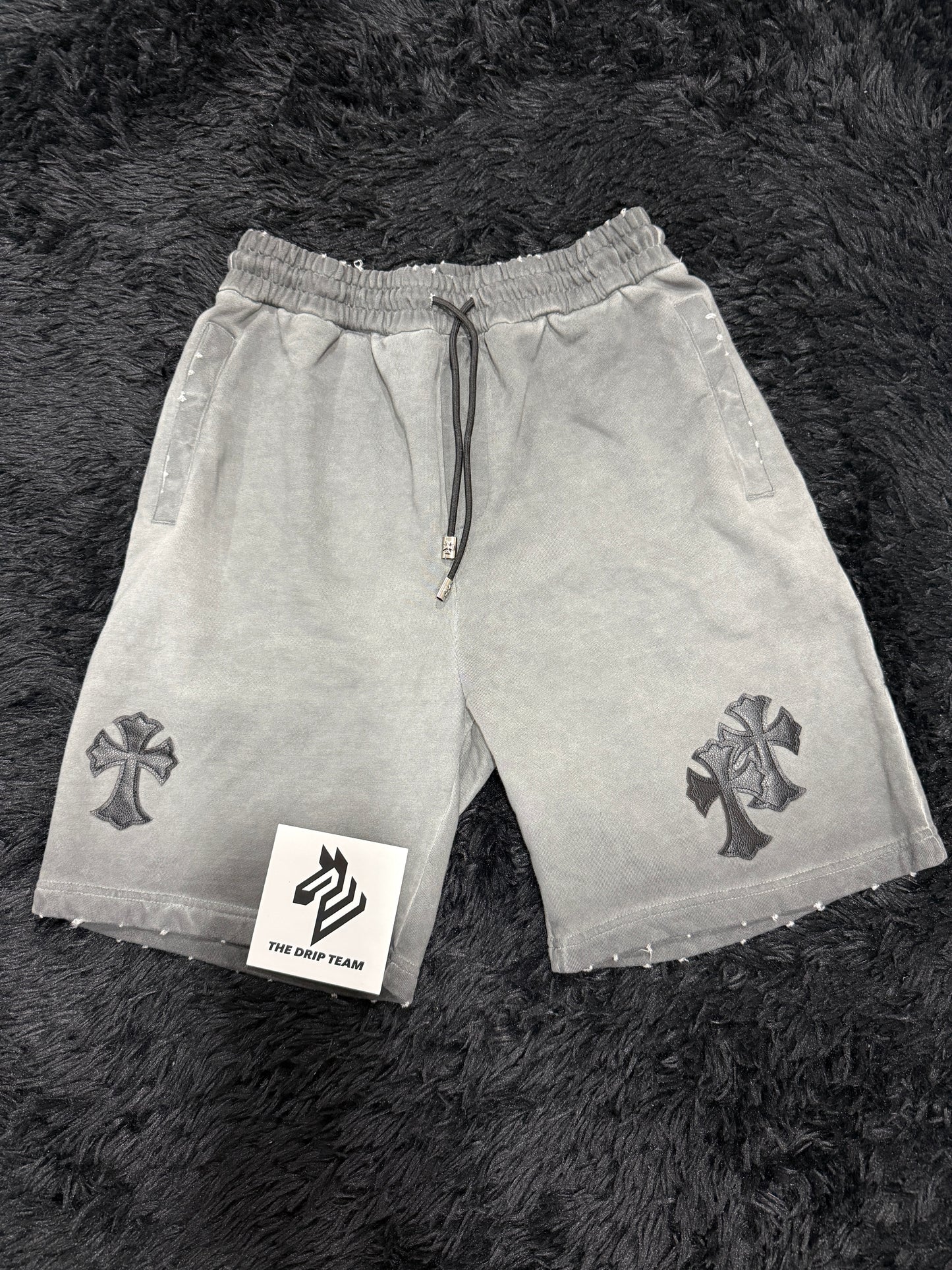 Gray Chrome Hearts shorts with a black cross design on a dark textured surface