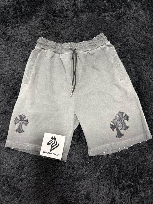 Gray Chrome Hearts shorts with a black cross design on a dark textured surface