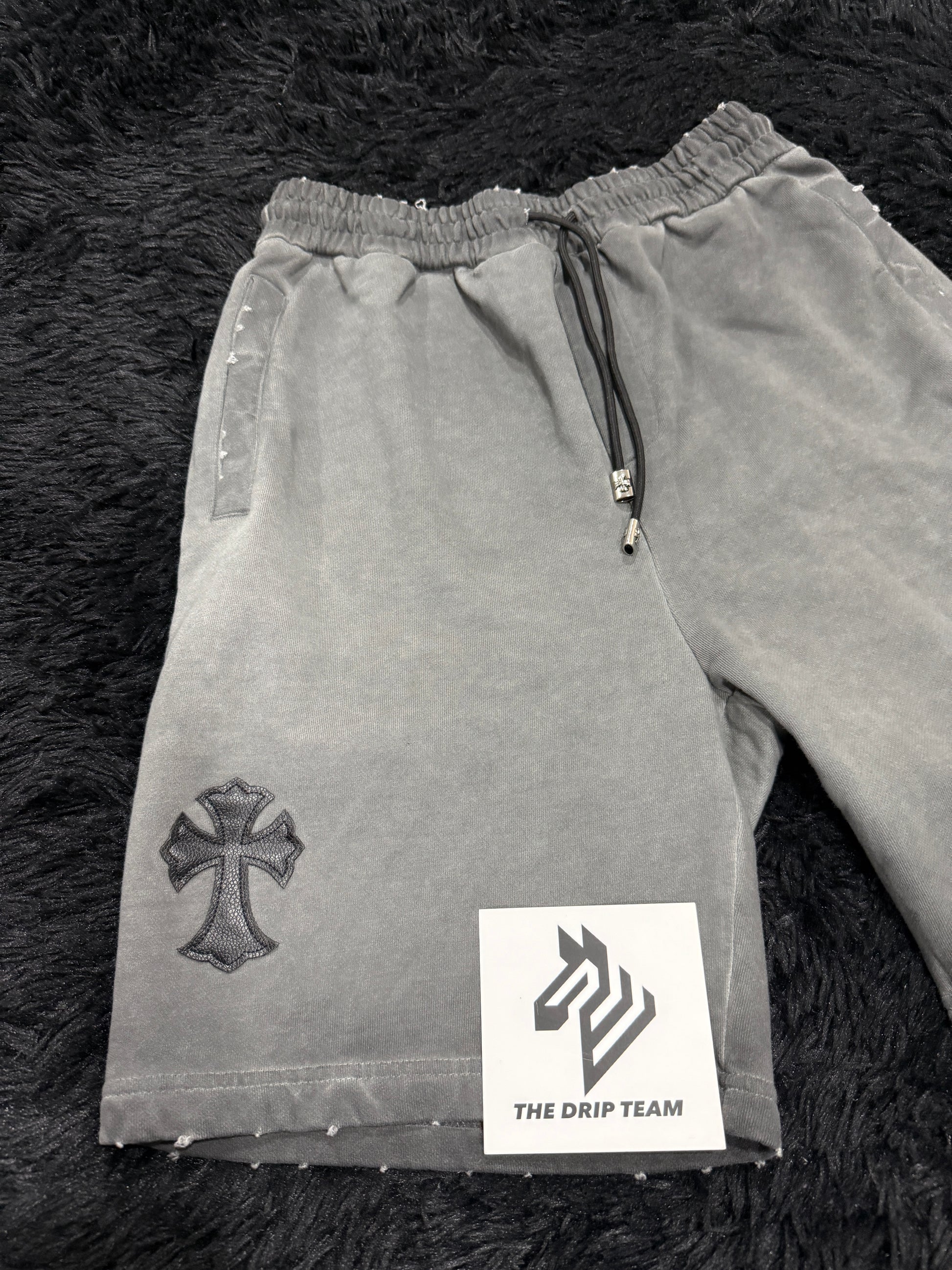 Gray Chrome Hearts shorts with a black cross design on a dark textured surface